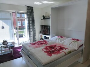 A bedroom with a bed, a TV, a bookshelf, and a sliding glass door to the outside. - Wohnung an der Lagune by Interhome (Büsum)