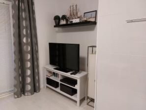 Ein Zimmer mit Fernseher auf einem weißen Schrank, einer kleinen Ablage mit Dekoration und einer Tür mit Vorhang.