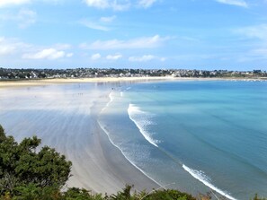 A beach with clear water, a sandy shore, and a town in the background. - La Ferme by Interhome (Saint Cast le Guildo)