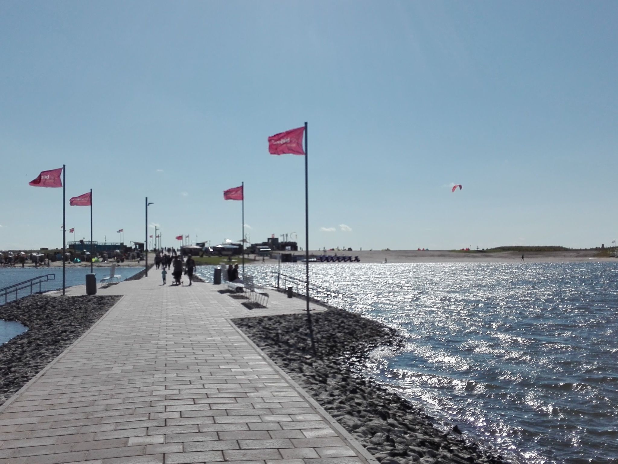 En asfalterad gångväg längs en strandpromenad, med flaggor och en klar himmel.