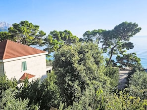 Ein Gebäude mit rotem Ziegeldach, umgeben von üppiger Vegetation und mit Blick auf ein Gewässer.