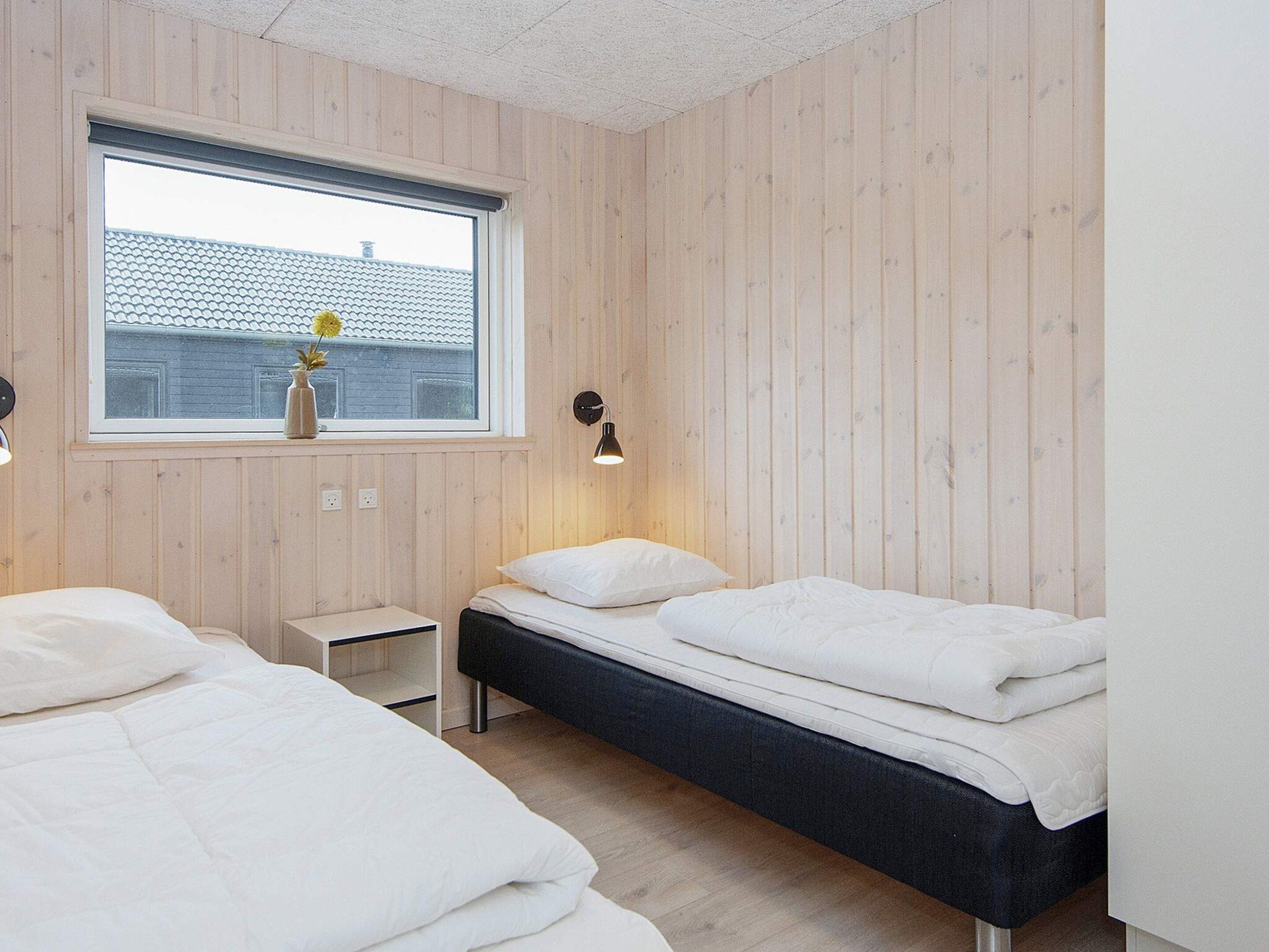 A bedroom with two beds, a window, and a bedside table with a lamp.