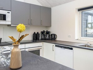 Eine moderne Küche mit grauen Schränken, einer Kaffeemaschine und einem Gelbes blühende Blume in einer Vase auf der Arbeitsplatte.