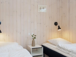 A room with two beds, a bedside table with a vase, a wall-mounted lamp, and a small framed picture. - Luxury Retreat With Pool (Rømø)