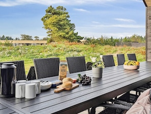 A wooden table with chairs, a coffee pot, mugs, biscuits, a bottle, a bowl of fruit, and a potted plant. - Luxury Retreat With Pool (Rømø)
