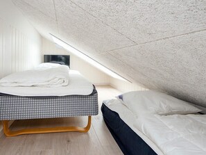 A bedroom with a sloped ceiling, a bed with a checkered bedspread, and a white pillow. - 18 Person Holiday Home in Romo (Rømø)