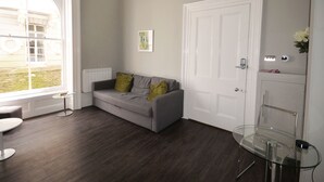 Een moderne woonkamer met een grijze bank, een glazen tafel en een witte deur.