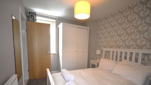 A bedroom with a bed, a nightstand, a lamp, a door, and a window. - in Torquay by Interhome (Torquay)