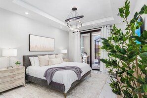 Ein modernes Schlafzimmer mit Bett, Nachttischen, einer Chandelüster, einem Gemälde und Blick ins Freie.