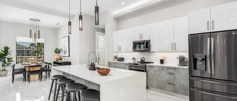 Una cocina moderna con una isla grande, electrodomésticos de acero inoxidable y un comedor con taburetes de bar.