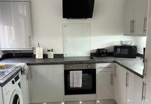 A compact kitchen with a washing machine, microwave, toaster, and a small oven. - House Sleeps 8 with Garden (Nottingham)