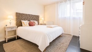 Ein Schlafzimmer mit einem großen Bett, zwei Nachttischen, einem Deckenventilator, einem Fenster mit durchsichtigen Vorhängen und einer Heizung.