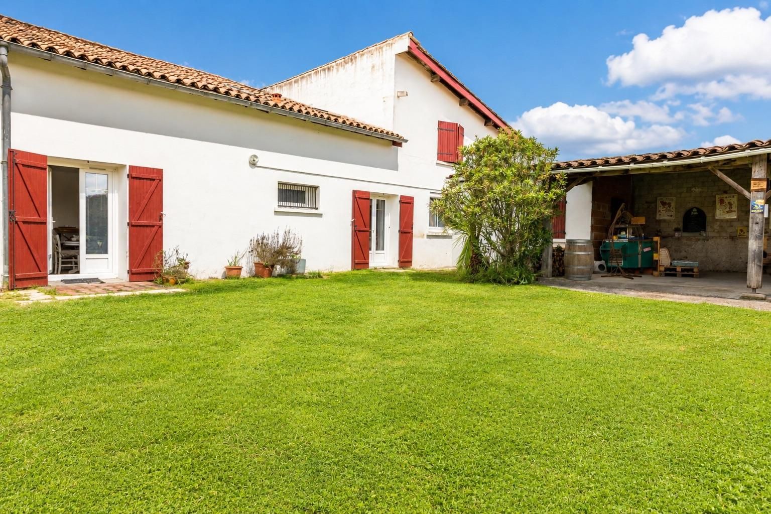 A white building with red shutters, a tiled roof, and a well-maintained lawn.