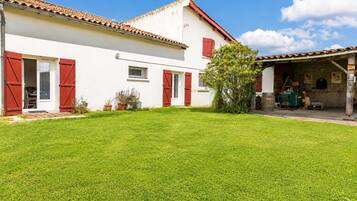 A white building with red shutters, a tiled roof, and a well-maintained lawn.