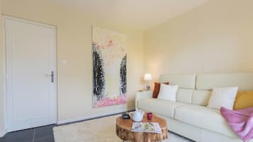 Un salon avec un canapé blanc, une table basse ronde, un tableau accroché au mur et une porte.