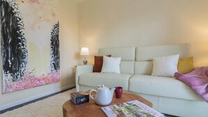 Ein Wohnzimmer mit einer Couch, einem Couchtisch mit Wasserkocher und Tasse, einer Lampe und einem großen Blumenbild.