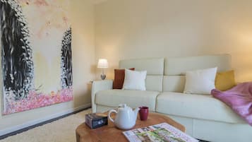 Un salon comprenant un canapé, une table basse avec une bouilloire et une tasse, une lampe et un grand tableau représentant des fleurs.