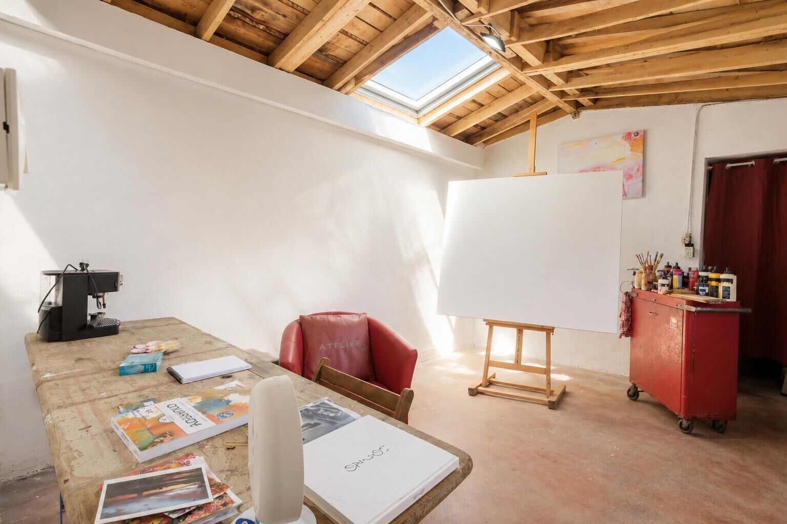 Ein Zimmer mit Holzboden, einem Oberlicht, einem roten Stuhl, einer Whiteboard-Tafel und einem roten Schrank mit Kunstbedarf.