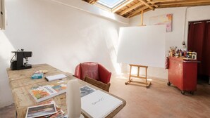 Ein Zimmer mit Holzboden, einem Oberlicht, einem roten Stuhl, einer Whiteboard-Tafel und einem roten Schrank mit Kunstbedarf.