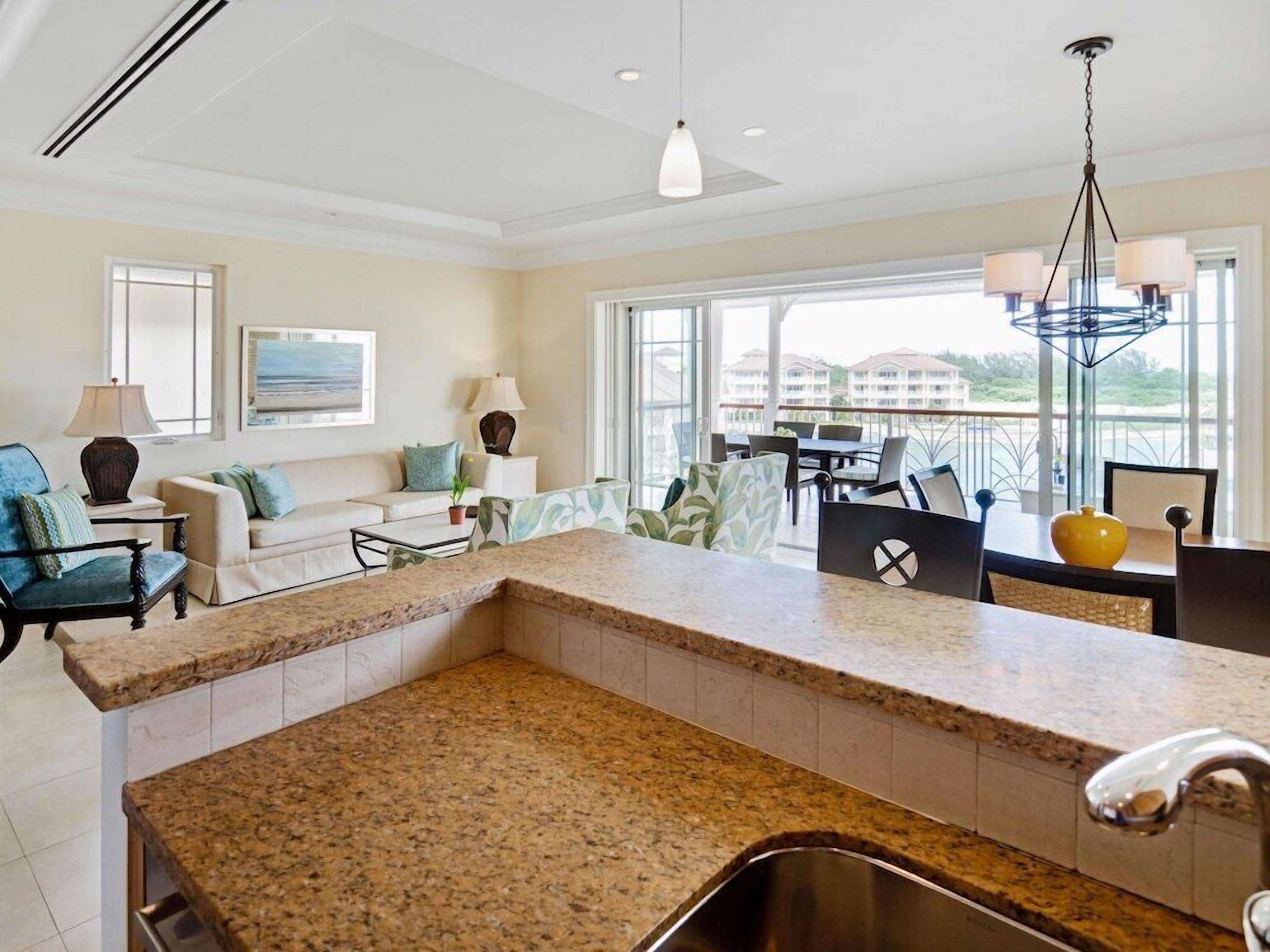 A modern kitchen with granite countertops, a dining area with a table and chairs, a sofa, and a balcony with a view.