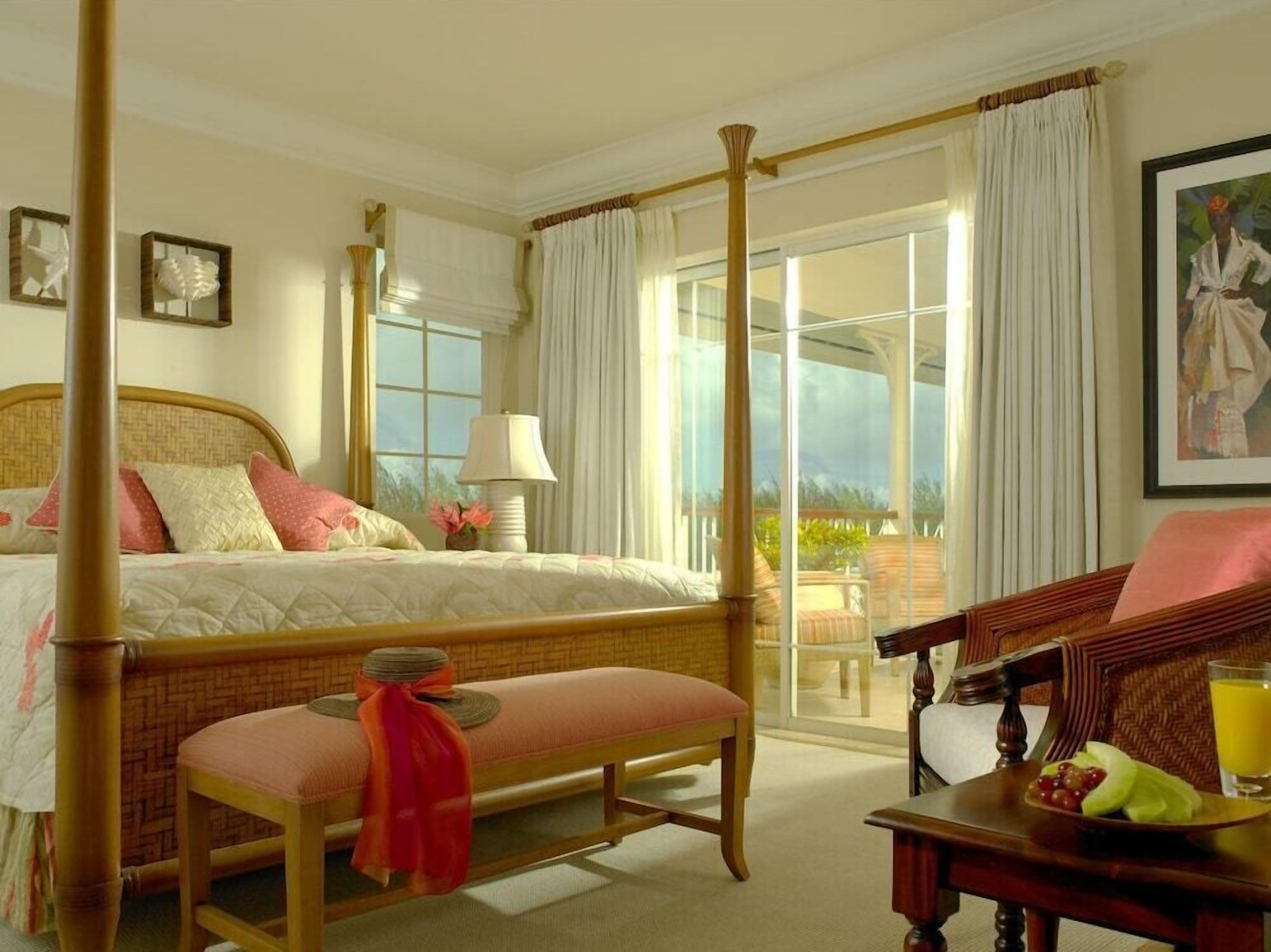 A four-poster bed, a bench, a table with fruit, and a balcony with a view.