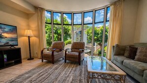 A living room with a large window, a sofa, two armchairs, a coffee table, and a TV. - Walk to beach, 3BR Beach Escape, Amazing Value (Lahaina)