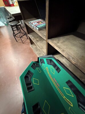 Una habitación con una mesa de juegos verde, estanterías de madera y una silla roja.