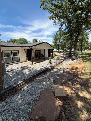 A house with a covered patio, a gravel driveway, and a stone pathway. - Your lakefront retreat with private boat slip, firepit, game room & wildlife ❤️ (Canadian)