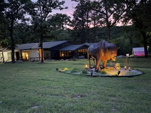 Un espacio al aire libre rústico con una gran escultura de animal, un pequeño estanque y un edificio de techo inclinado.