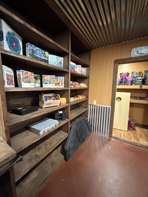 A room with wooden shelving containing various board games and puzzles. - Your lakefront retreat with private boat slip, firepit, game room & wildlife ❤️ (Canadian)
