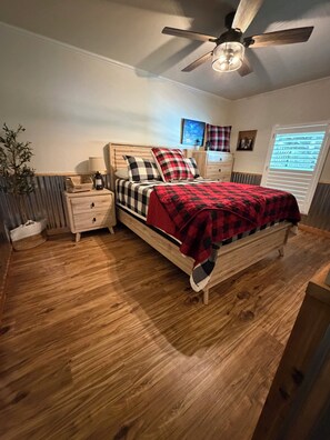 A bedroom with a wooden bed, a nightstand, a ceiling fan, and a window with blinds.