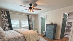 Ein Schlafzimmer mit einem Bett, einem Deckenventilator, einem Schminktisch und einem begehbaren Kleiderschrank.