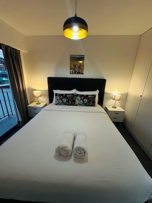 Ein Hotelzimmer mit einem Bett, zwei Nachttischlampen, einem Bild an der Wand und Blick nach draußen.