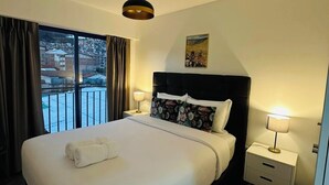 Habitación de hotel con una cama grande, vista a la ciudad por la ventana, un cuadro en la pared y una lámpara en el techo.