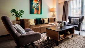 Una sala de estar moderna con un sofá, un sillón, una mesa de centro y un cuadro de un llama.