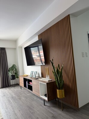 Ein modernes Wohnzimmer mit einem flachbildfernseher an der Wand, einem Holzkonsole mit einem Topfpflanzen und einem großen Fenster mit Vorhängen.