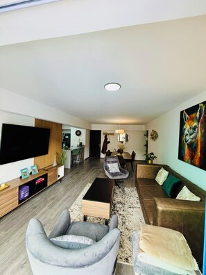 Ein modernes Wohnzimmer mit Fernseher, grauem Sessel, braunem Sofa und einem großen Lammgemälde.