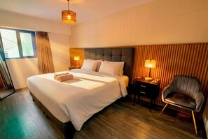 Ein Hotelzimmer mit einem großen Bett, Nachttischen, einem Sessel, einem Fenster mit Vorhängen und einem Holzboden.