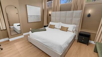 Une chambre à coucher avec un grand lit, un miroir, une table de chevet et une fenêtre avec des rideaux.