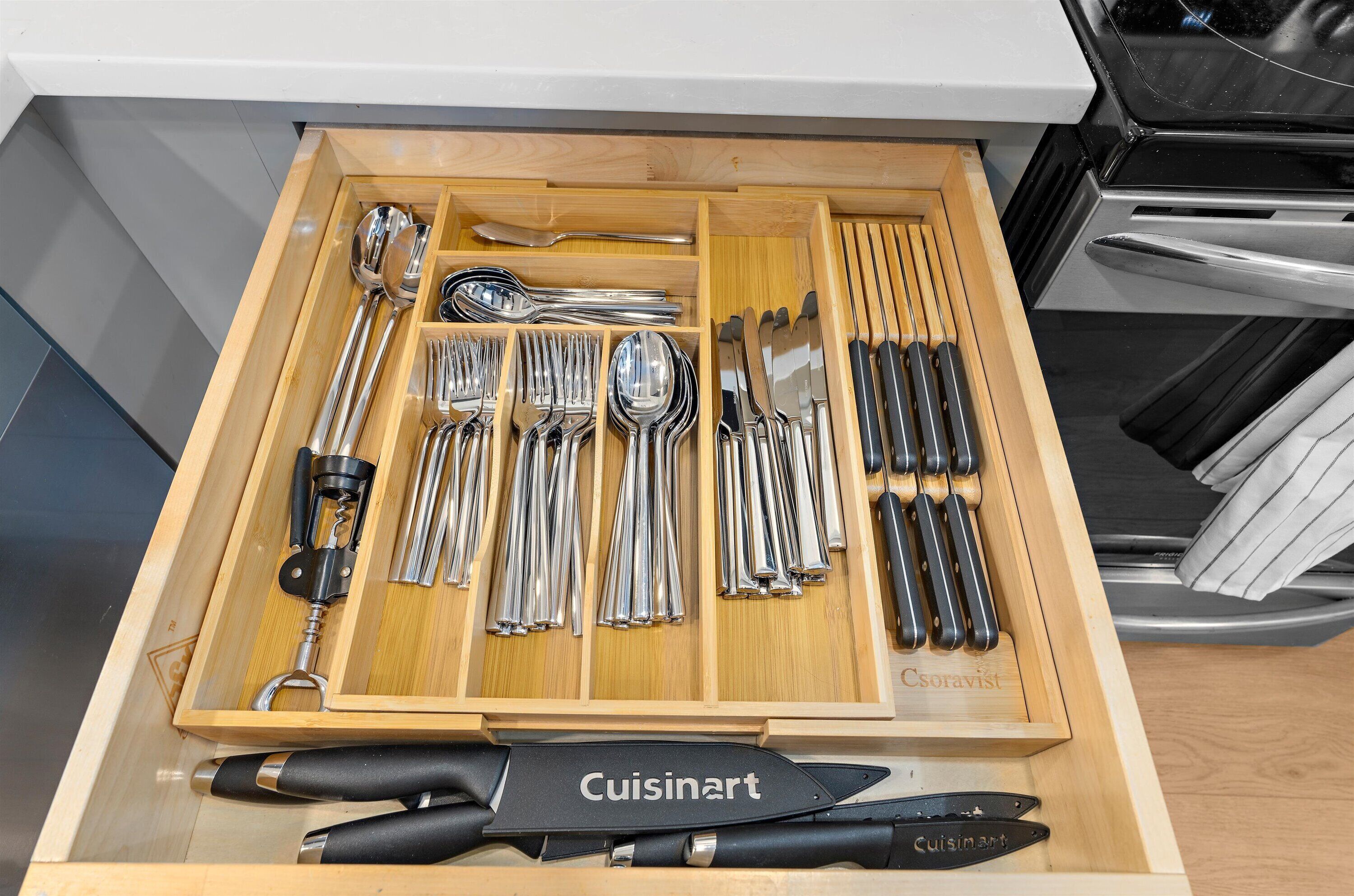 Un tiroir contenant divers ustensiles et outils de cuisine, notamment des cuillères, des fourchettes, des couteaux et un tire-bouchon.