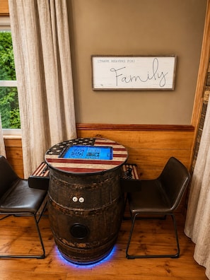 Une table en forme de baril en bois ornée d’un motif représentant le drapeau américain, deux chaises noires et un panneau accroché au mur sur lequel on peut lire : « Merci au ciel pour la famille. »