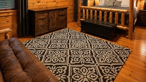 Ein Holzblockhaus-Interieur mit Holzbalkendecke, einem aufgehängten Hirschgeweih, einem Bett mit hölzernem Gestell, einem an der Wand montierten Fernseher und einem gemusterten Teppich.