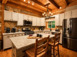 A kitchen with granite countertops, white cabinets, a stainless steel refrigerator, and a stone wall. - Beautiful & Perfectly Located Cabin w/ Hot Tub + Bunk Room + Game Room (Gatlinburg)