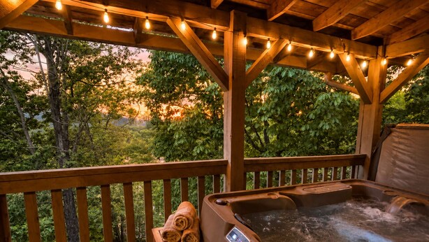 Eine Holzterrasse mit Whirlpool, einem Sessel mit Handtüchern und Lichterketten.