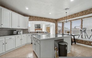 A kitchen with white cabinets, a central island, and a stone accent wall. - The Castle LuX Family Retreat Pool Home Theatre (DeSoto)