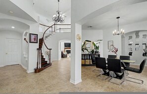 A spacious living area with a staircase, a dining area with a table and chairs, and a kitchen in the background. - The Castle LuX Family Retreat Pool Home Theatre (DeSoto)