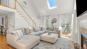 Un salon spacieux avec un canapé d’angle, une cheminée, un escalier et une lucarne.