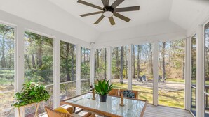 Une terrasse couverte avec une table en verre, des chaises en osier et un ventilateur de plafond.