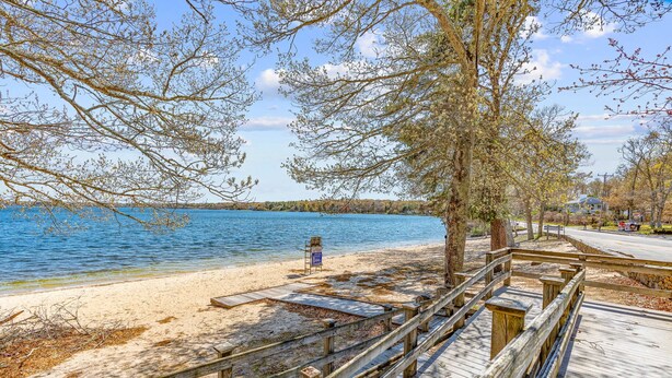 Une plage avec une promenade en bois, un banc et un panneau situé près de l’eau.