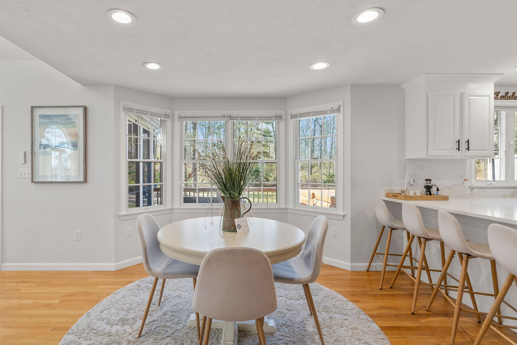 A modern kitchen with a round dining table, bar stools, large windows, and a view of the outdoors.